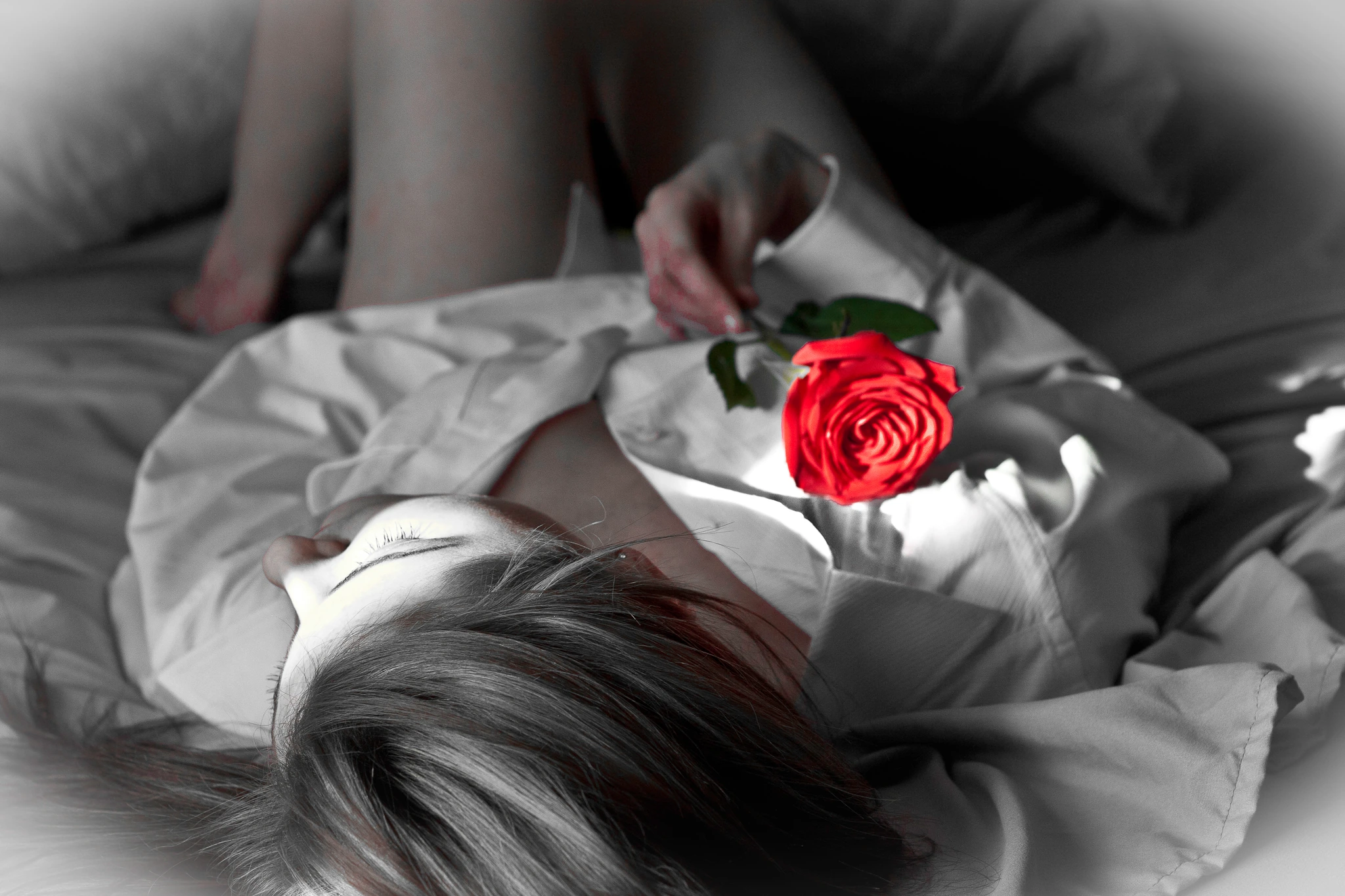 A bride resting with a single red rose in her hand, the frame black and white but for the flower